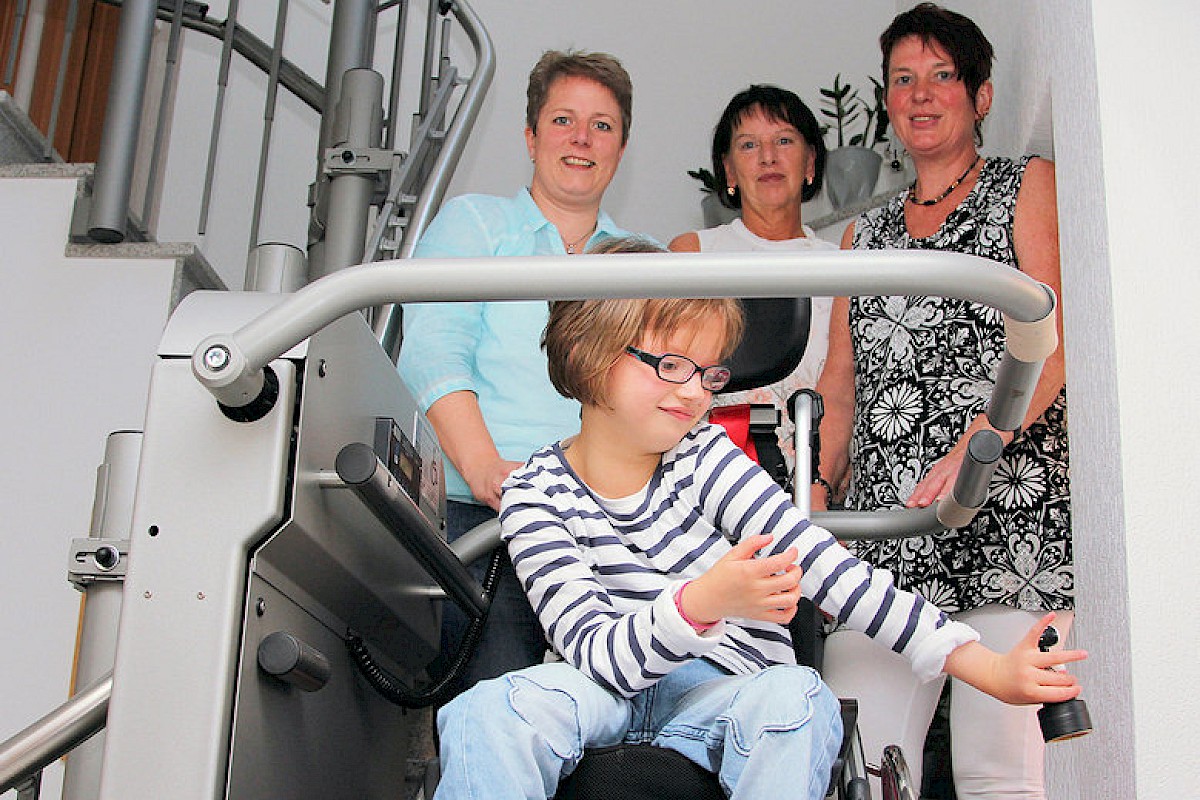 Andrea Bremer zeigt Angelika Möllmann und Ulrike Stork (v.l.), wie gern ihre Tochter Lilly mit dem Treppenlift fährt. Foto: Peppenhorst